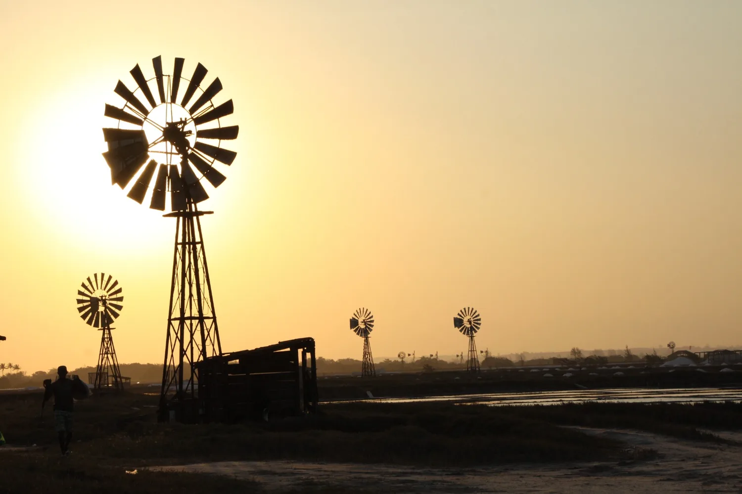 Cataventos das salinas ao entardecer, com trabalhador carregando sal